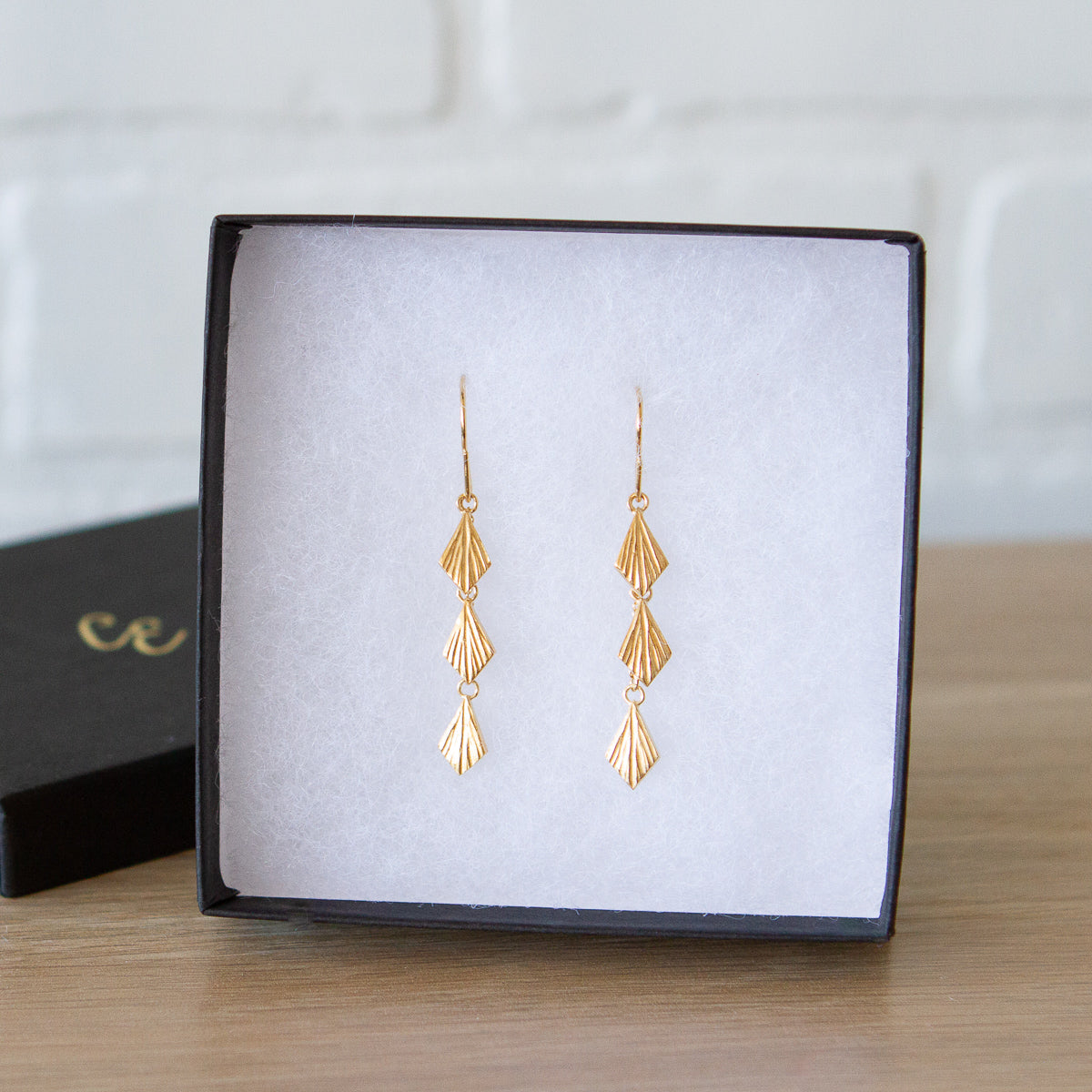 Three overlapping cascading tiers of fan-shaped flame dangles in gold vermeil hanging from an earwire in a gift box