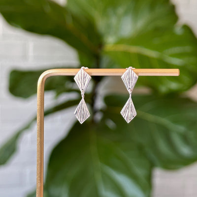 Double Silver Flame Dangle Earrings hanging in front of a white wall, front angle