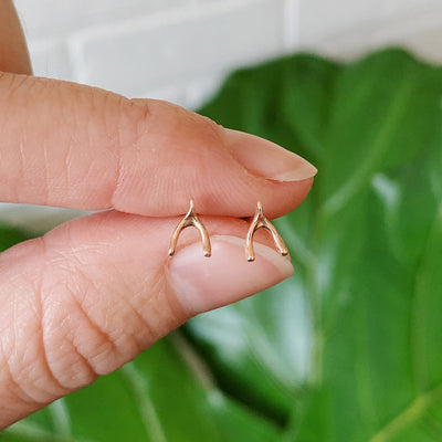 rose gold wishbone stud earrings held between two fingers