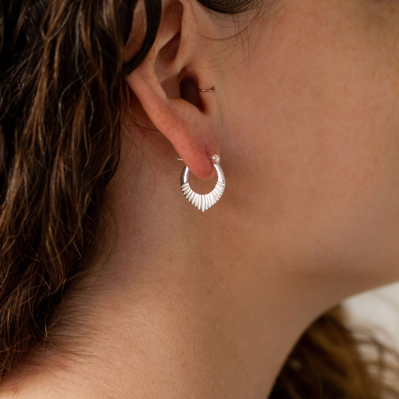 Silver Small Oblong hoops with hinge closure and sunburst bottom by Corey Egan on an ear