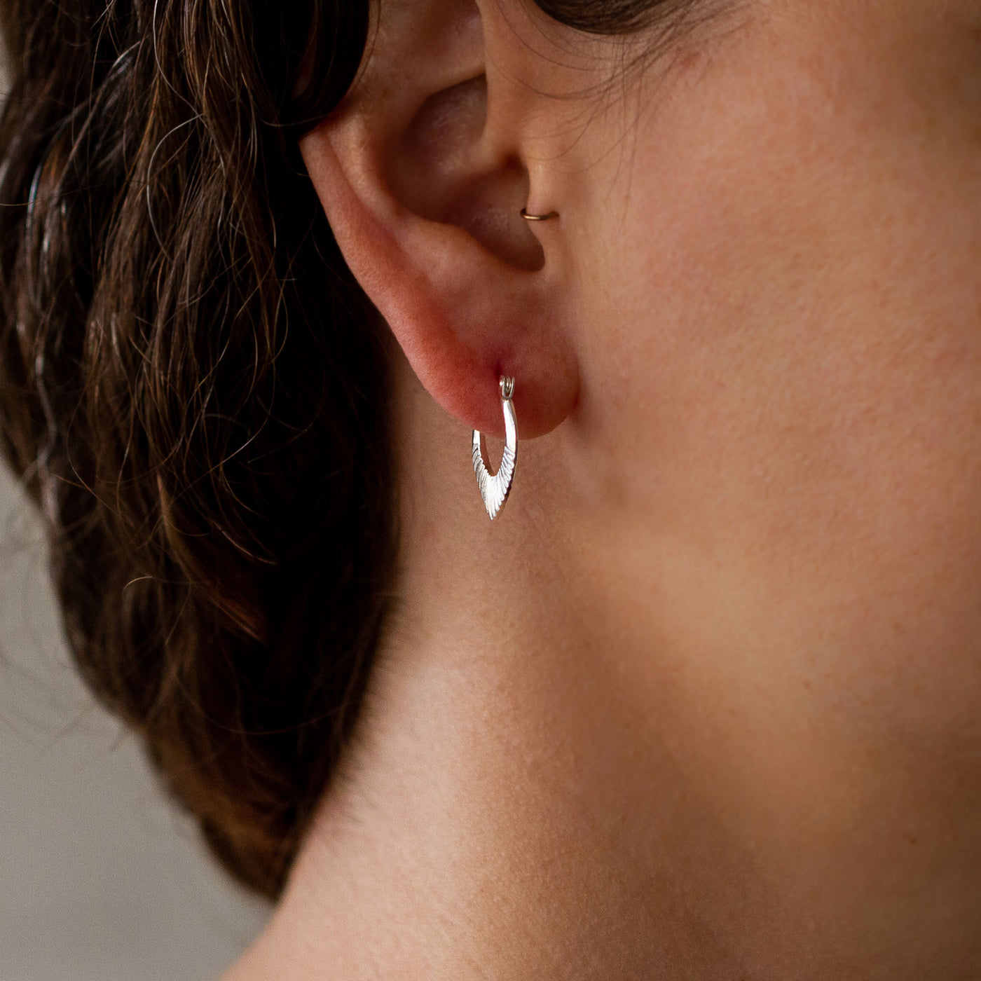 Silver Small Oblong hoops with hinge closure and sunburst bottom by Corey Egan on an ear alternate view