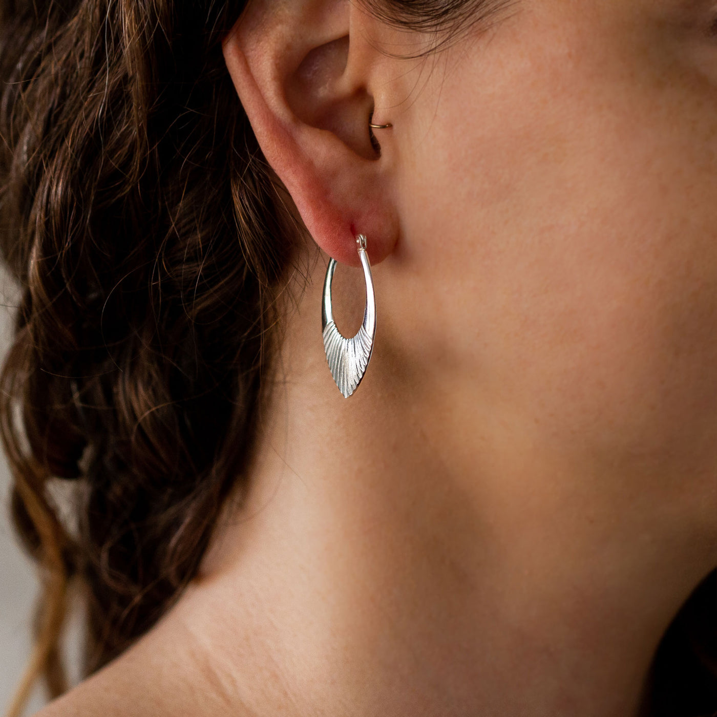 Medium Silver Oblong hoops with hinge closure and sunburst bottom by Corey Egan on an ear