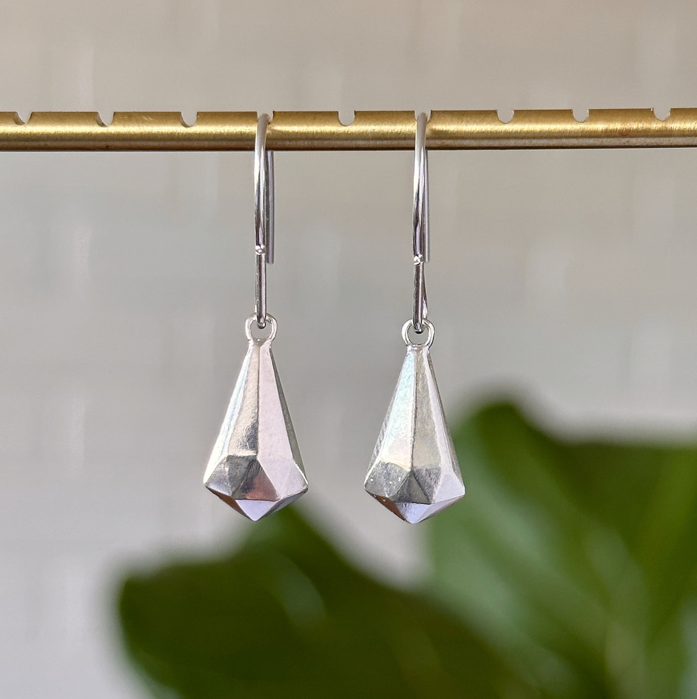 Silver Crystal Fragment Earrings hanging in front of a white wall, front angle