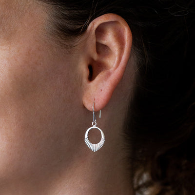silver small open petal shape earrings with textured bottoms on an ear