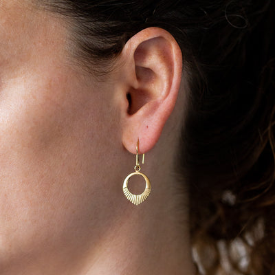 Gold vermeil small open petal shape earrings with sunburst bottoms on an ear