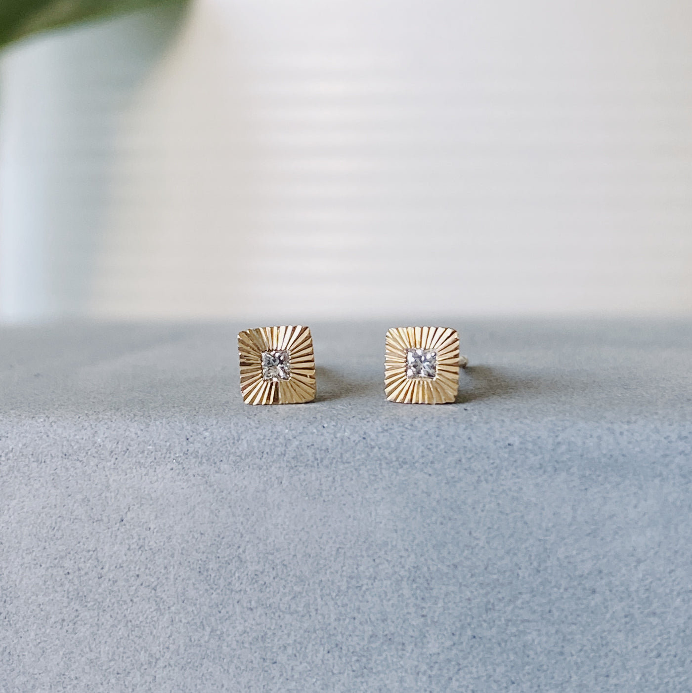 Square 14k yellow gold Aurora stud earrings with princess cut diamond centers and engraved rays in natural light