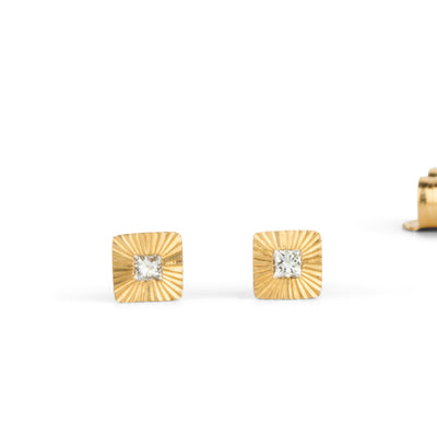 Square 14k yellow gold Aurora stud earrings with princess cut diamond centers and engraved rays on a white background