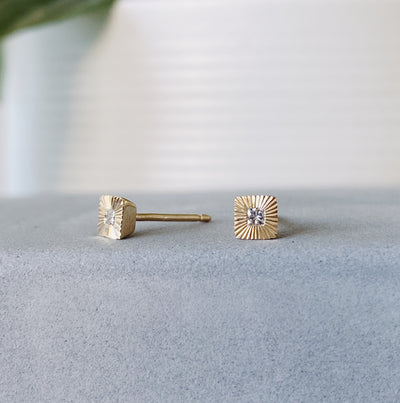 Square 14k yellow gold Aurora stud earrings with princess cut diamond centers and engraved rays in natural light side view