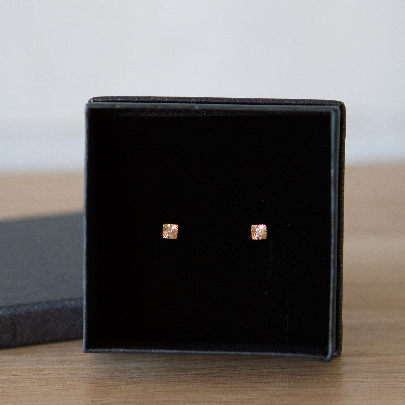 Square 14k yellow gold Aurora stud earrings with princess cut diamond centers and engraved rays in a gift box