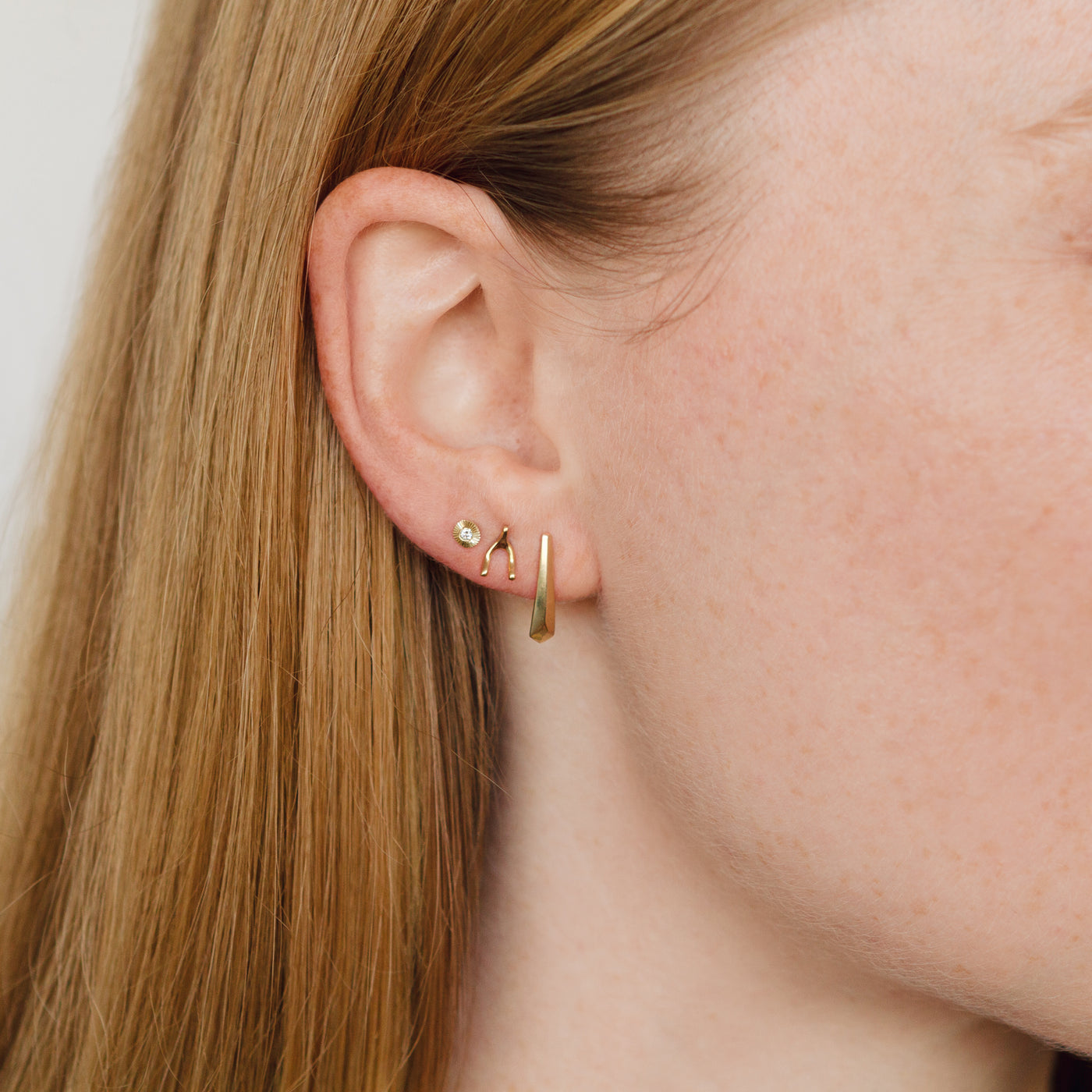 Gold wishbone stud earrings with gold and diamond micro aurora stud earrings and gold tapered fragment studs on an ear