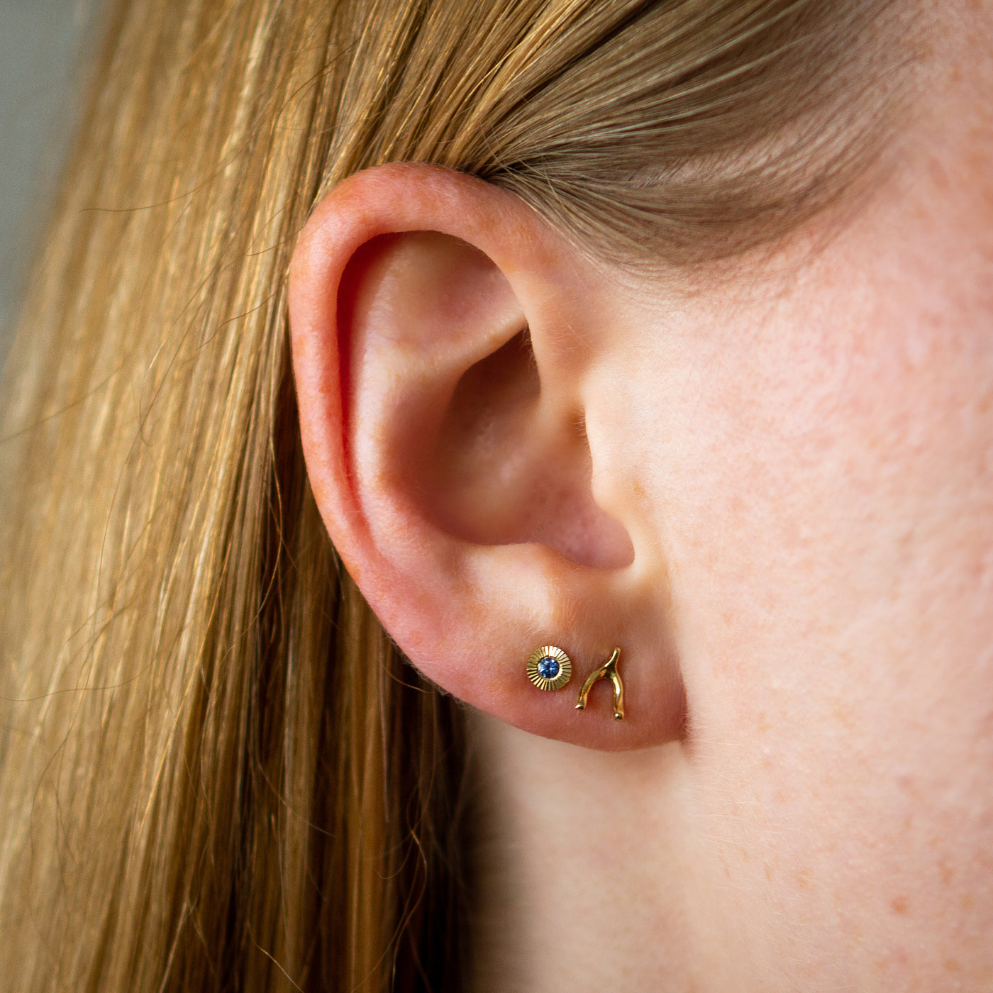 Gold and blue yogo sapphire aurora stud earrings with gold wishbone stud earrings on an ear
