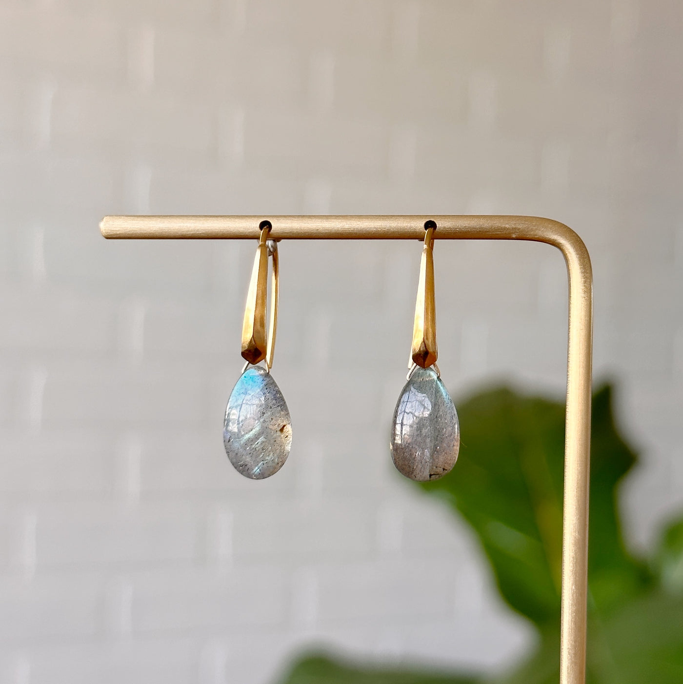 Labradorite earrings in gold vermeil hanging on gold stand in front of a white wall, front angle