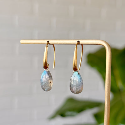Labradorite earrings in gold vermeil hanging on gold stand in front of a white wall, side angle