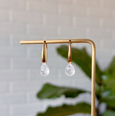 Moonstone earrings in gold vermeil hanging on gold stand in front of a white wall, front angle