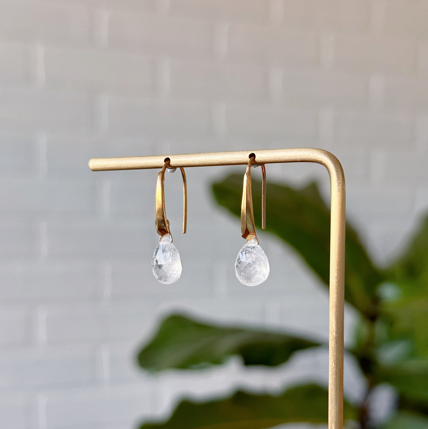 Moonstone earrings in gold vermeil hanging on gold stand in front of a white wall, side angle