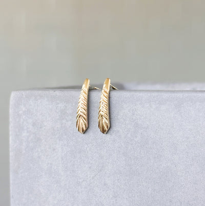 Yellow Gold Tapered Herringbone Stud Earrings hanging on a concrete wall, side angle