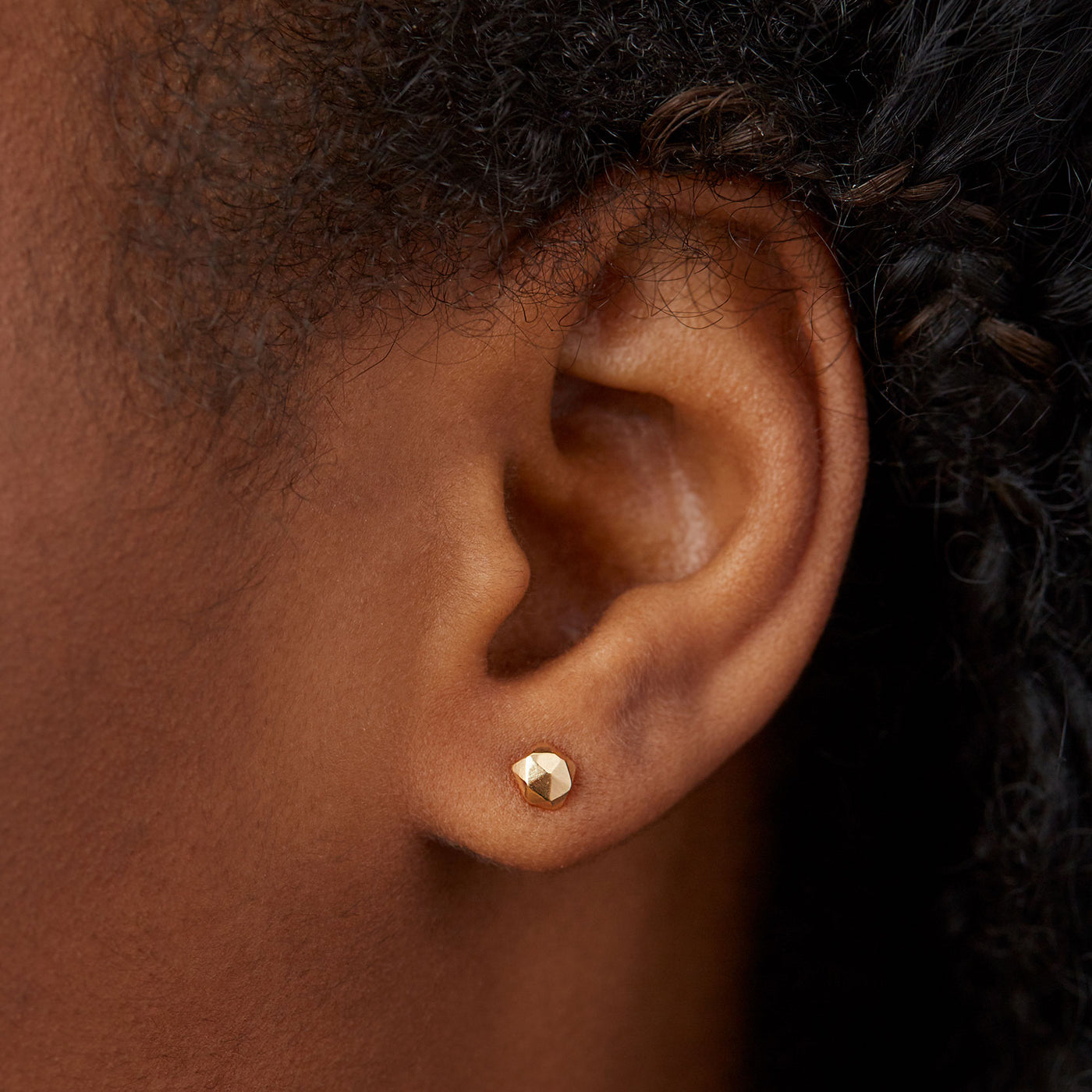 14k yellow gold geometric faceted stud earrings in the micro size on an ear by Corey Egan