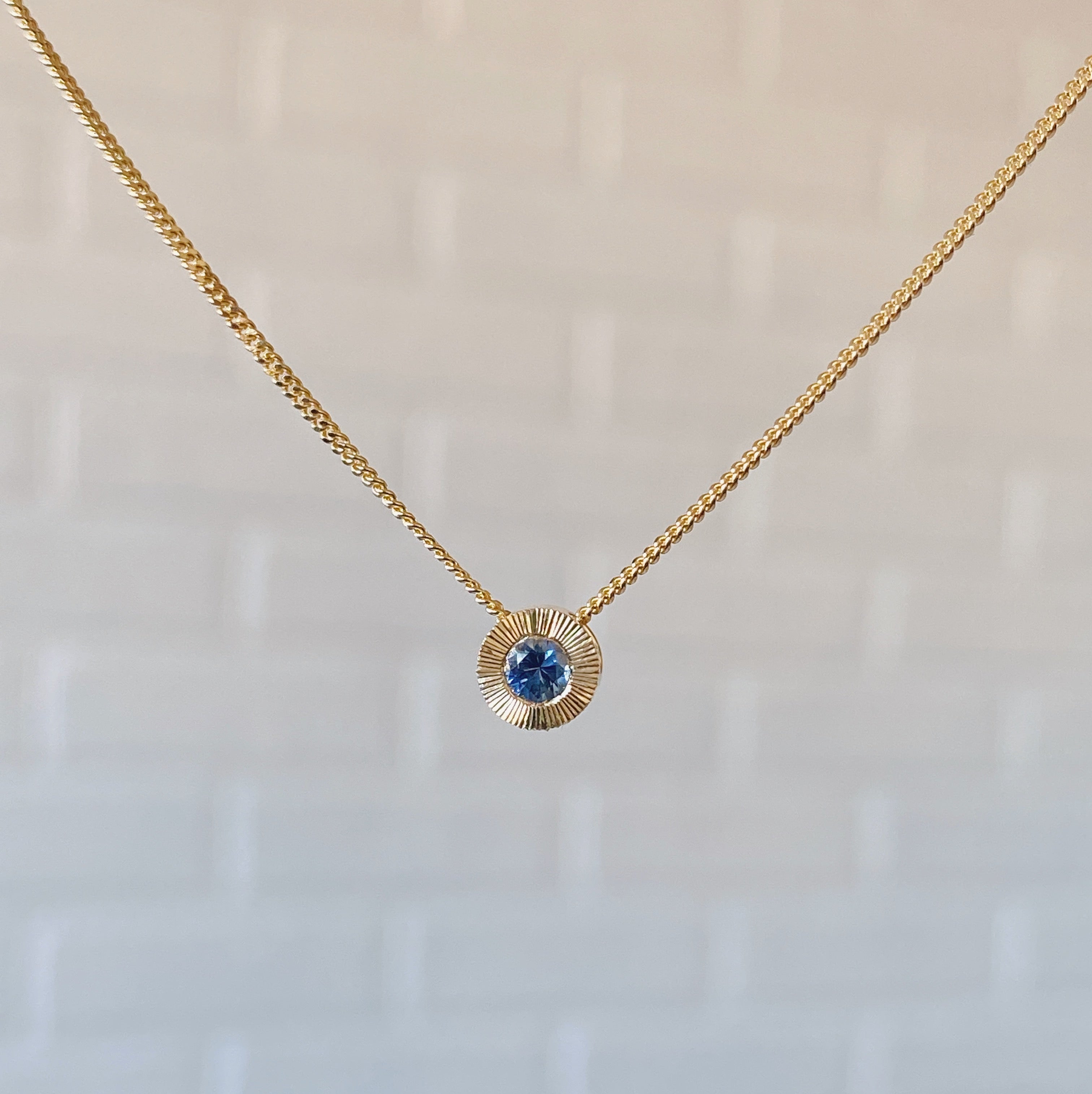 14k yellow gold small aurora necklace with a blue montana sapphire center in natural light