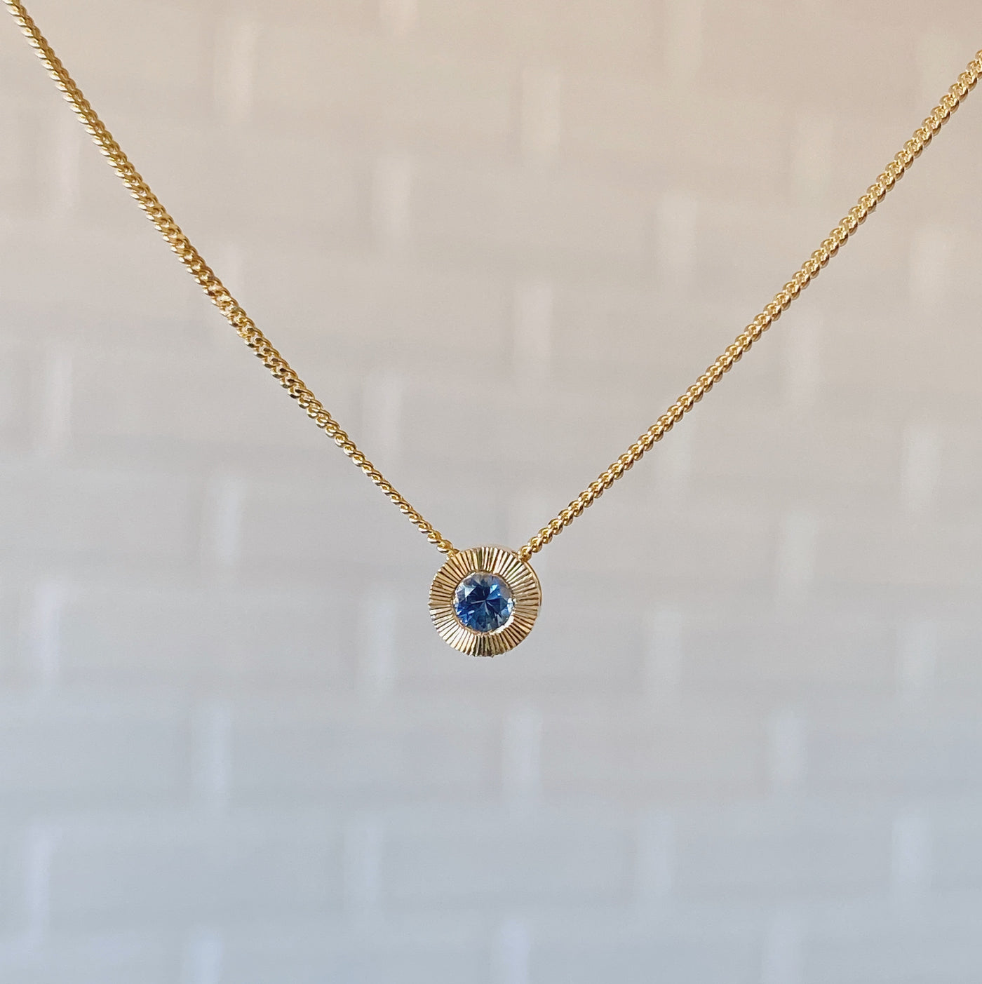 14k yellow gold small aurora necklace with a blue montana sapphire center in natural light