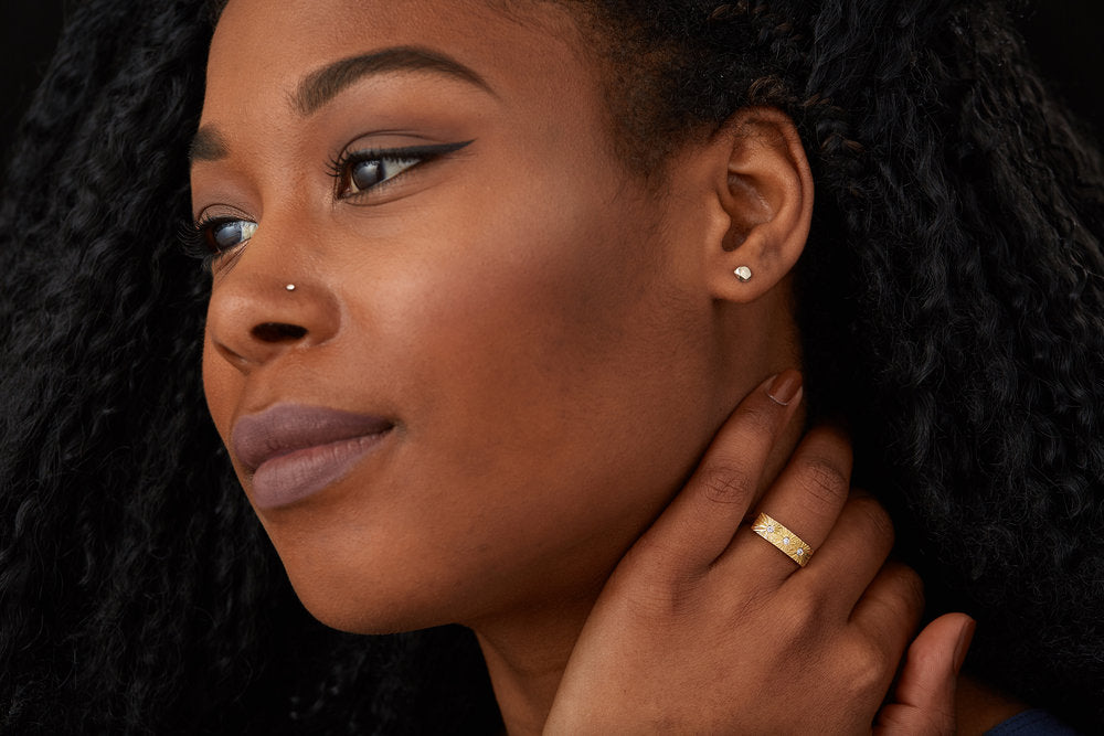 Yellow gold bar ring with three diamonds and a carved sunburst design around each by Corey Egan on a model