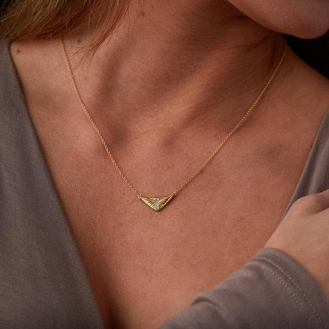 Triangular gold flash necklaw eith a diamond center and sunburst carved motif in 14k yellow gold around a neck by Corey Egan
