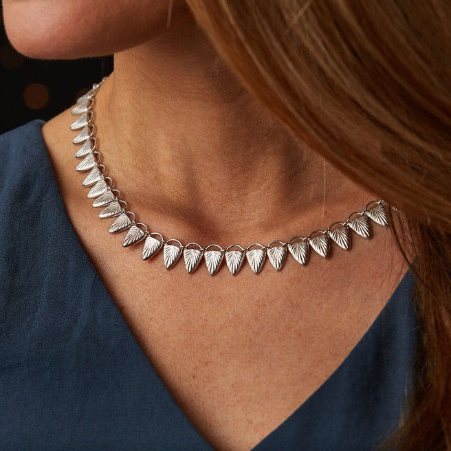 Sterling silver statement necklace made of triangular carved links with a sunburst design on a neck | Corey Egan