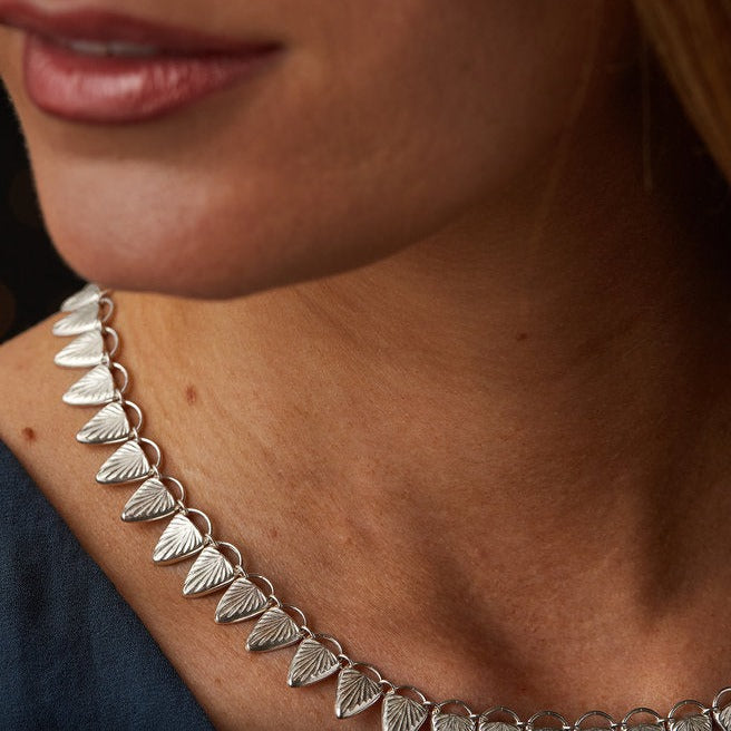 Sterling silver statement necklace made of triangular carved links with a sunburst design close up on a neck| Corey Egan