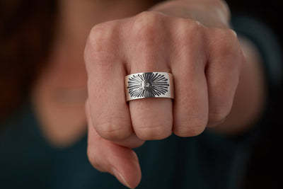 Oxidized silver wide band with single diamond and a carved sunburst design on a model by Corey Egan