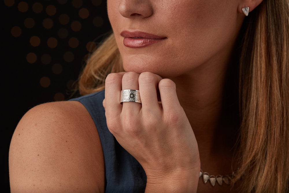 Sterling silver wide band with single diamond and a carved sunburst design on a model by Corey Egan
