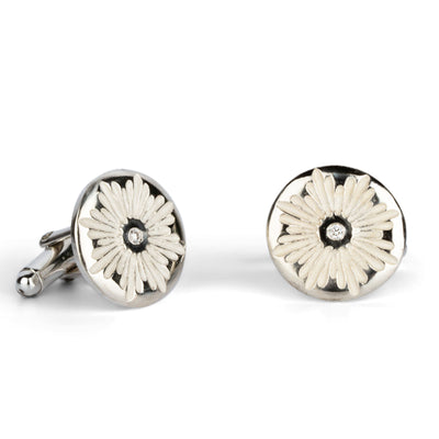 Side view of sterling silver round cufflinks with a floral carved sunburst design and diamond centers on a white background