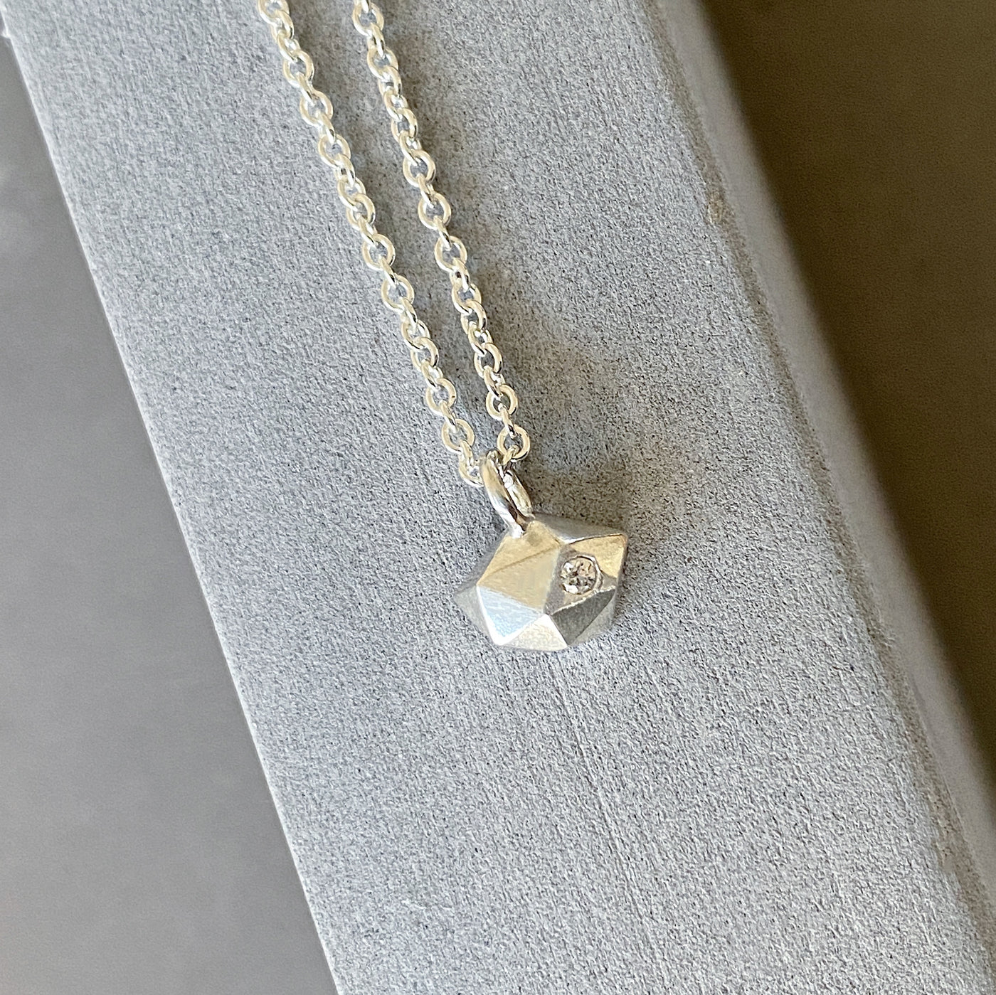 Sterling silver wabi-sabi faceted geometric necklace with a single diamond facet by Corey Egan on concrete