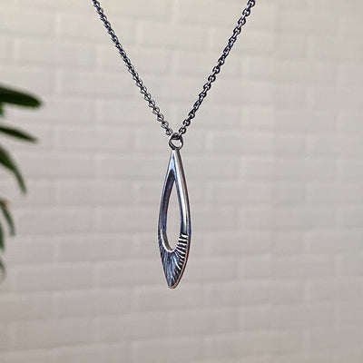 Side view of Oblong petal shaped pendant with a carved sunburst texture in oxidized sterling silver