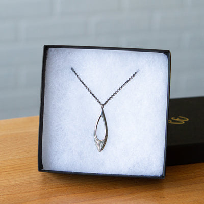 Oblong petal shaped pendant with a carved sunburst texture in oxidized sterling silver in a gift box