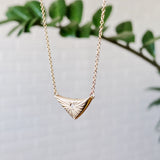 Triangular gold flash necklaw eith a diamond center and sunburst carved motif in 14k yellow gold side view in natural light. by Corey Egan