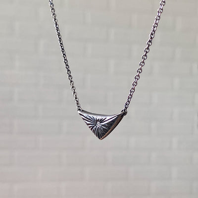 Side view of Triangle oxidized silver flash necklace with carved rays motif and a single center diamond