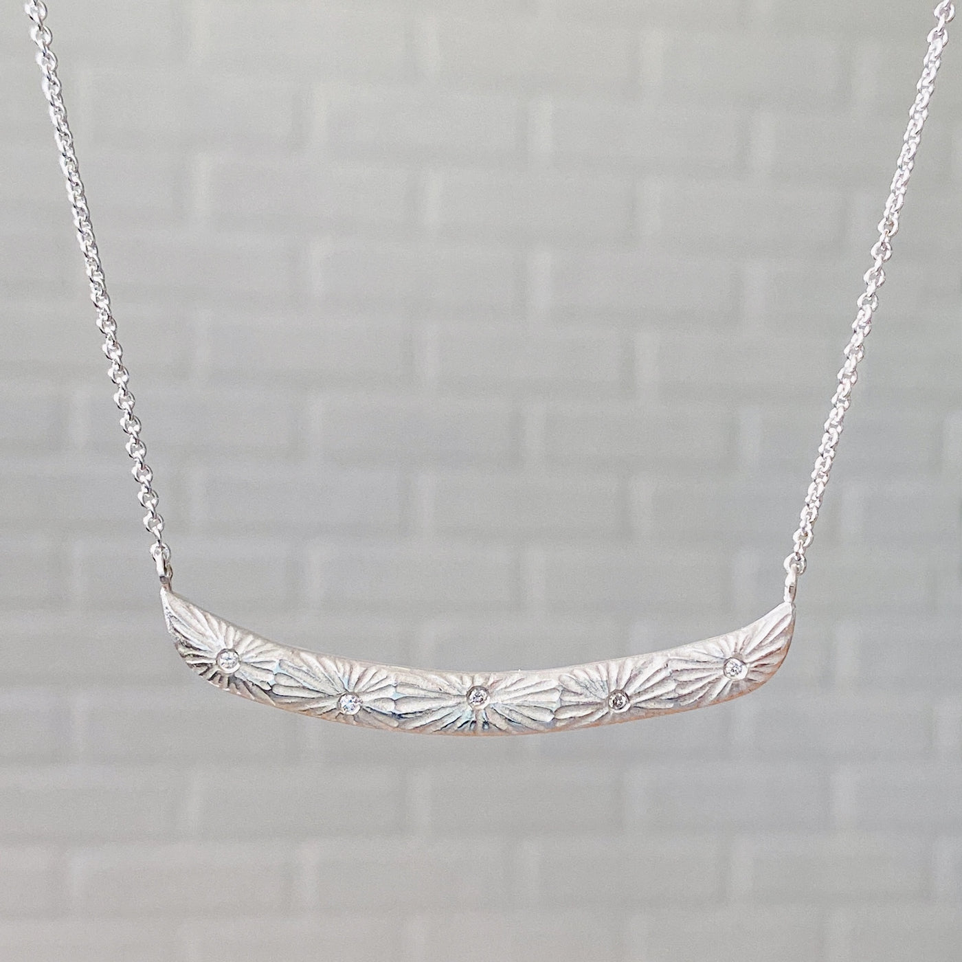 Sterling silver curved bar necklace with five scattered diamonds and an engraved sunburst pattern radiating from each in natural light | Corey Egan