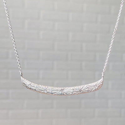Sterling silver curved bar necklace with five scattered diamonds and an engraved sunburst pattern radiating from each in natural light | Corey Egan