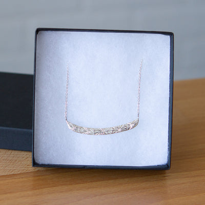 Sterling silver curved bar necklace with five scattered diamonds and an engraved sunburst pattern radiating from each in a gift box | Corey Egan