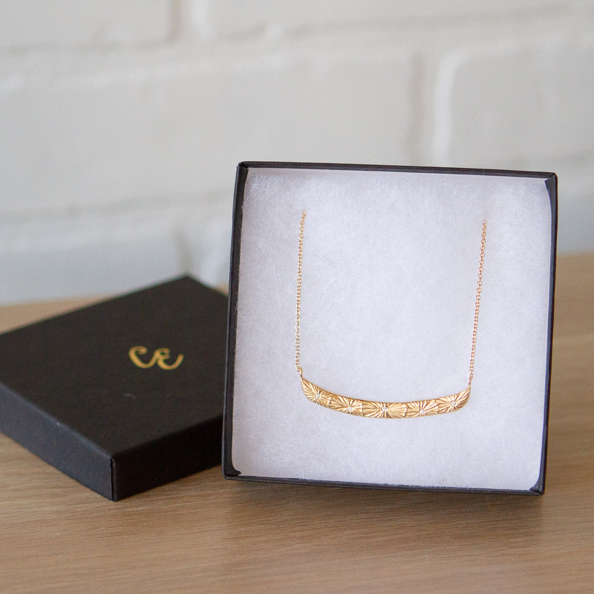 Curved bar necklace with five scattered diamonds and carved sunburst motif in a gift box by Corey Egan
