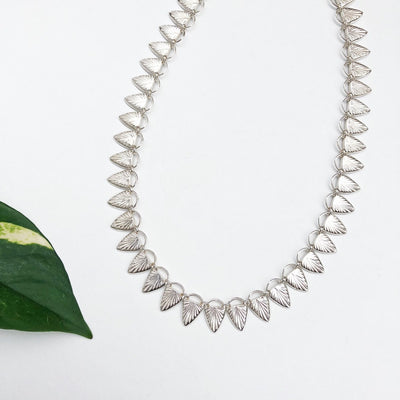 Sterling silver statement necklace made of triangular carved links with a sunburst design in natural light | Corey Egan