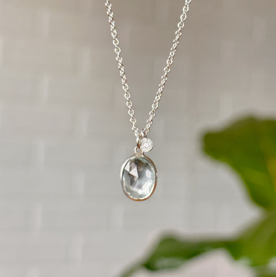Oval aquamarine pendant necklace in silver in front of a white wall, front angle