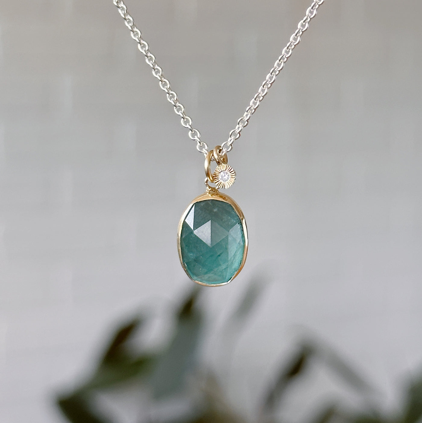 Oval Rose cut Grandidierite Silver and Gold Theia Necklace #4 hanging in front of a white wall, front angle
