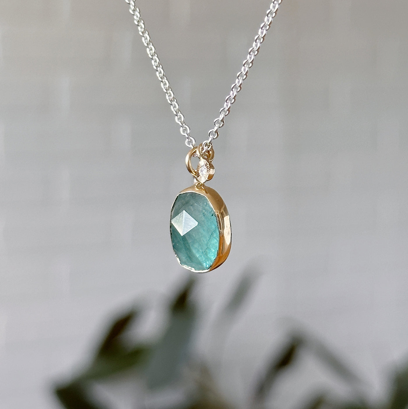 Oval Rose cut Grandidierite Silver and Gold Theia Necklace #4 hanging in front of a white wall, side angle