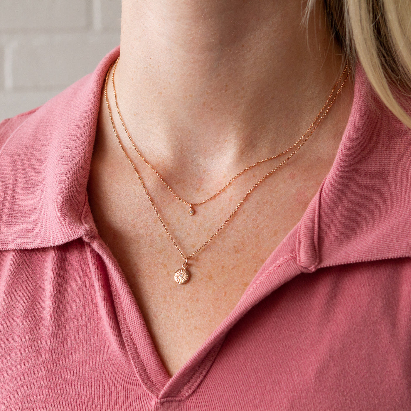 A model wears a 14k rose gold lucia neckalce paired with a rose gold rise necklace and a pink polo shirt
