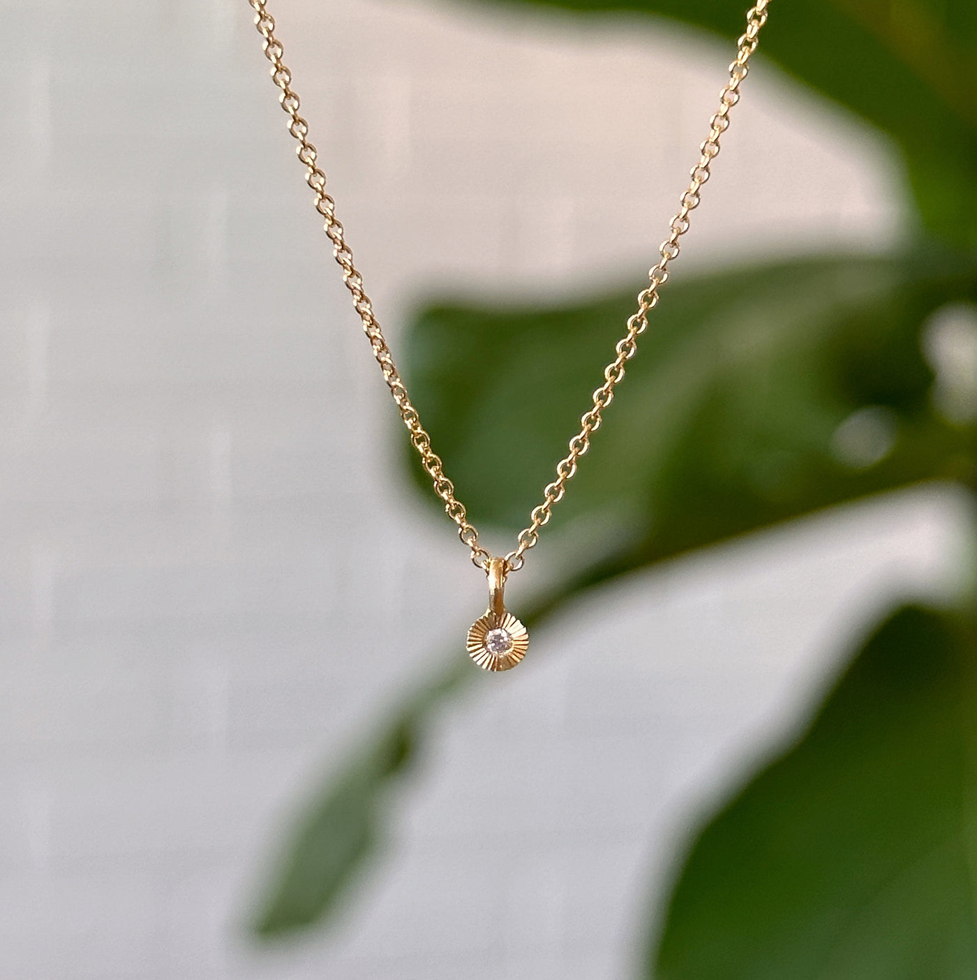 Gold and Diamond Rise Necklace hanging in front of a white wall, front angle