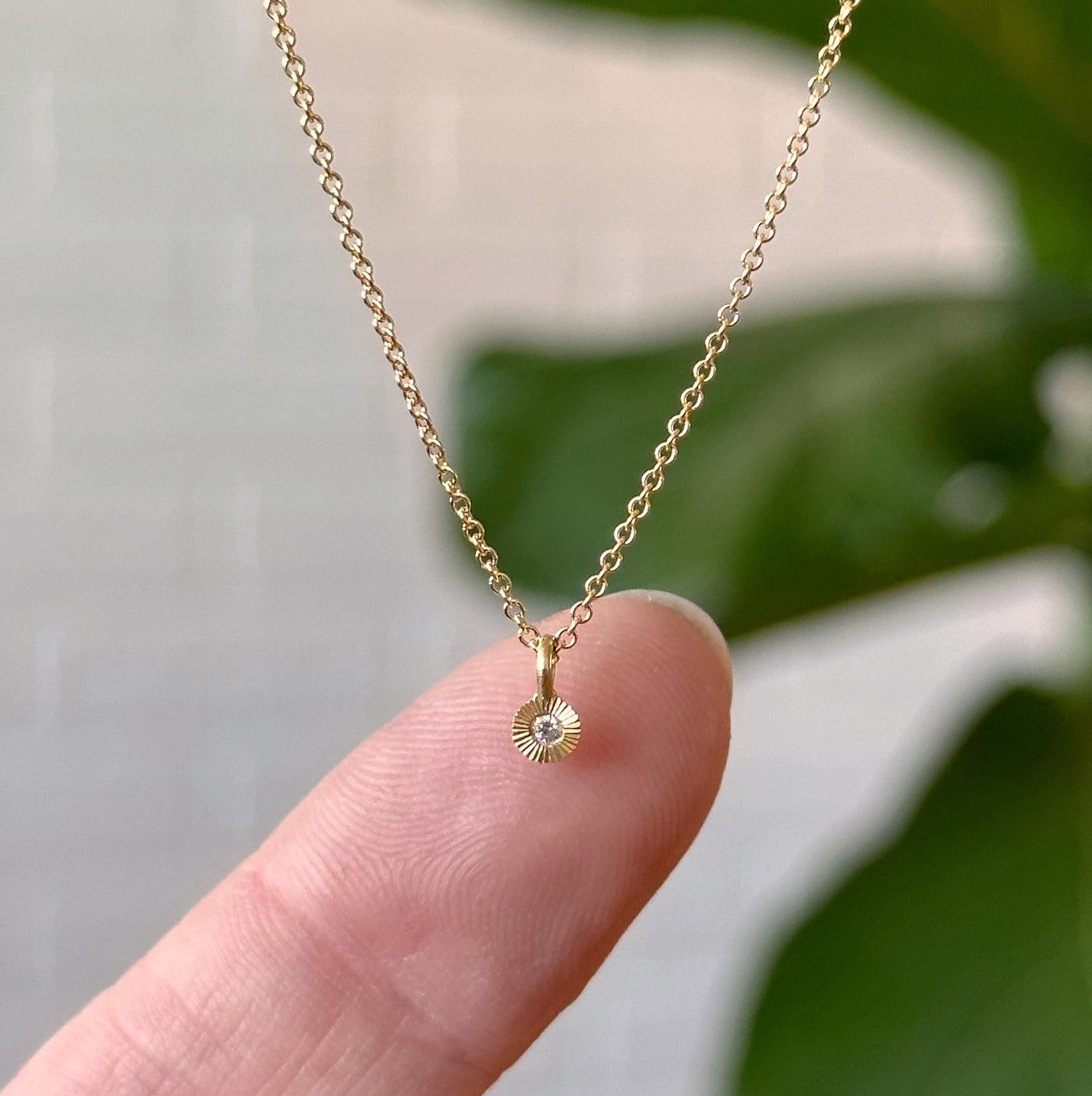Gold and Diamond Rise Necklace hanging in front of a white wall with finger in picture for scale