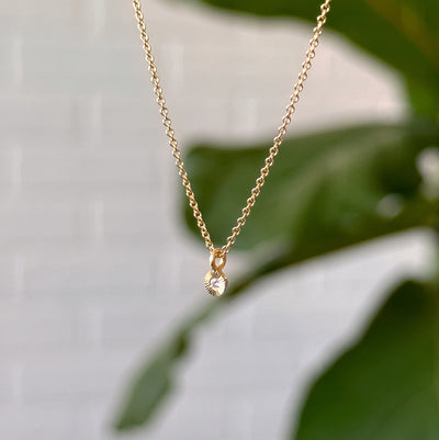 Gold and Diamond Rise Necklace hanging in front of a white wall, side angle
