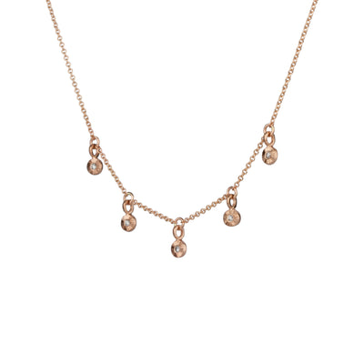 Side view Rose gold and diamond station necklace with five tiny engraved pendants with diamond centers on a white background
