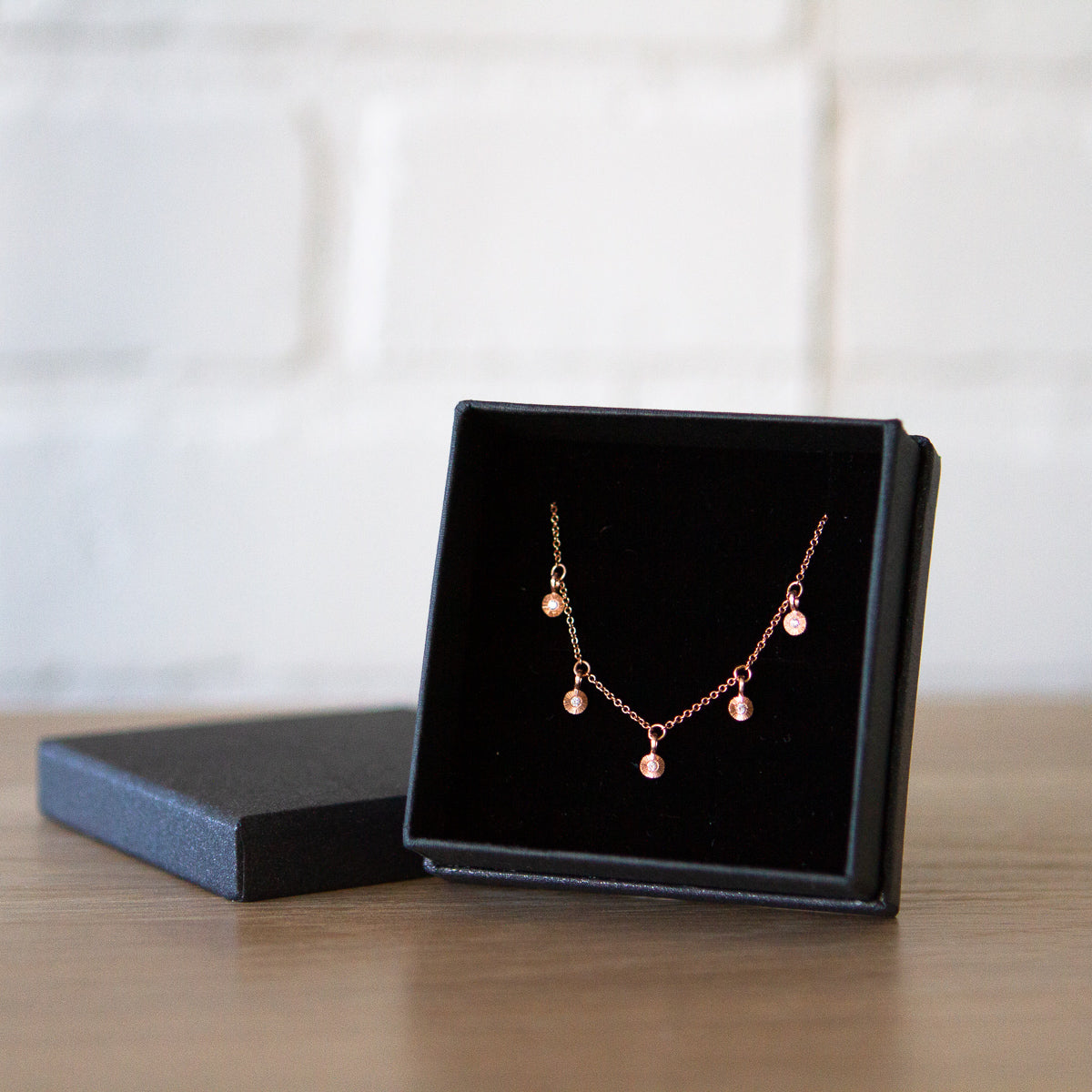 Rose gold and diamond station necklace with five tiny engraved pendants with diamond centers in a gift box