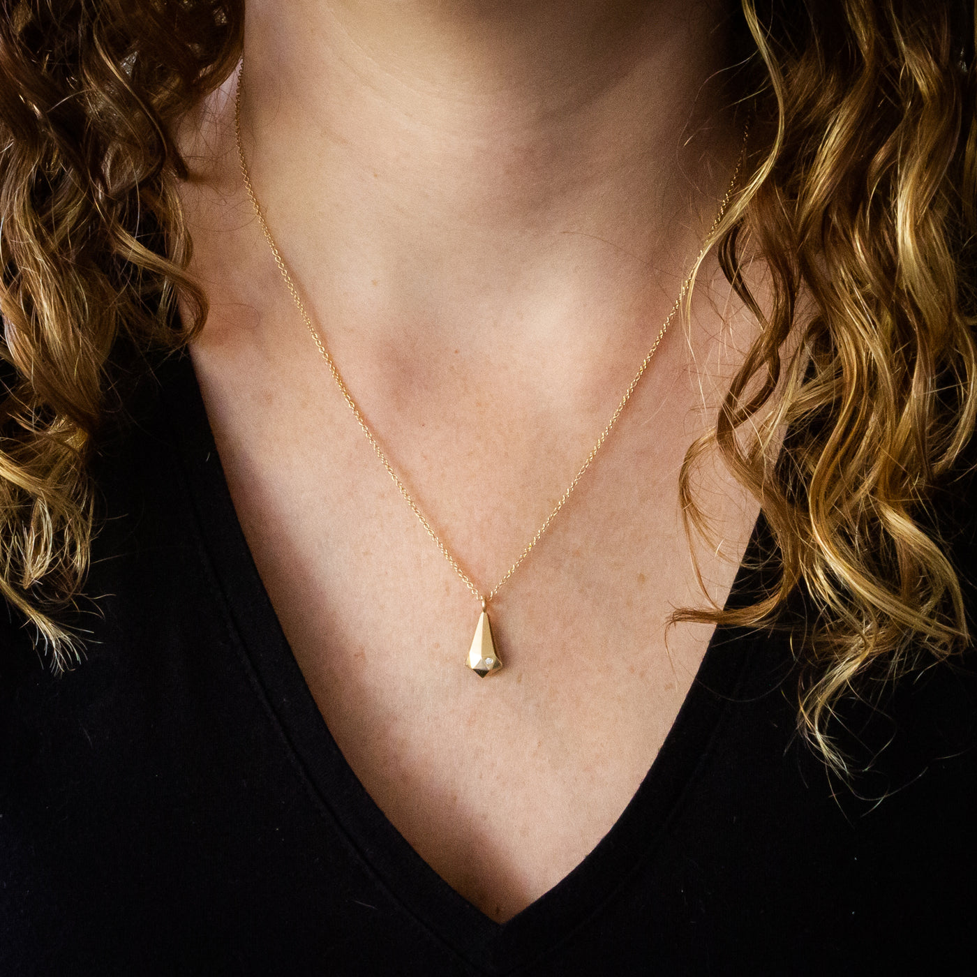 14k yellow gold faceted crystal fragment pendant with a diamond and a gold chain around a neck